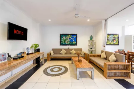 Cozy tropical living room with wooden sofas, Netflix on wall TV, and lush plant decor. - Bali Villas
