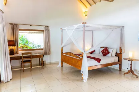 Serene tropical bedroom with wooden canopy bed, red accents, desk, and large windows overlooking greenery.