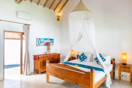 Cozy Balinese bedroom with wooden four-poster bed under white mosquito net canopy, turquoise bedding, and open doors to tropical outdoors.