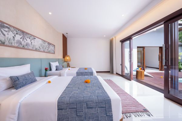 Spacious Balinese twin bedroom with white beds, frangipani accents, sliding doors to lush outdoor pool terrace.