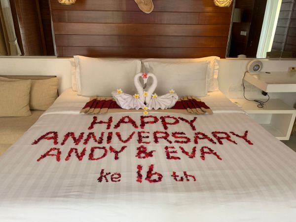 Romantic hotel bed decorated with swan-shaped towels and red rose petals spelling "Happy 16th Anniversary Andy & Eva". - Bali Villas