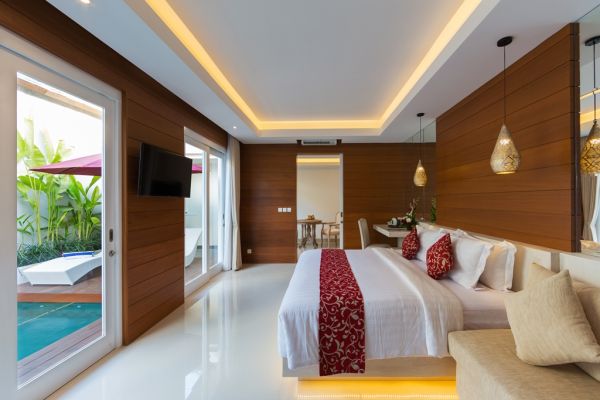 Luxurious tropical villa bedroom with king bed, wooden accents, and sliding doors to private infinity pool.