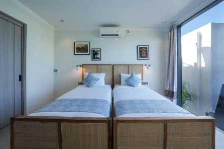 Serene minimalist bedroom with two wooden twin beds, white duvets, and large window overlooking tropical outdoors.