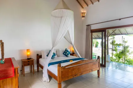 Spacious Balinese bedroom with wooden four-poster bed, white mosquito net canopy, and sliding doors opening to tropical garden view.