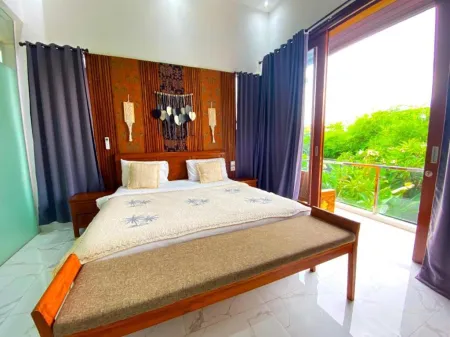 Cozy tropical bedroom with king-size wooden bed, macrame wall decor, purple curtains, and open balcony overlooking lush green vegetation. - Bali Villas