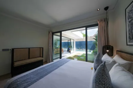 Spacious tropical villa bedroom with king bed, open sliding doors to private infinity pool, and lush garden view.