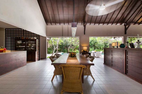 Spacious Balinese villa dining room with wooden beams, rattan furniture, open doors to lush garden, and tropical decor. - Bali Villas