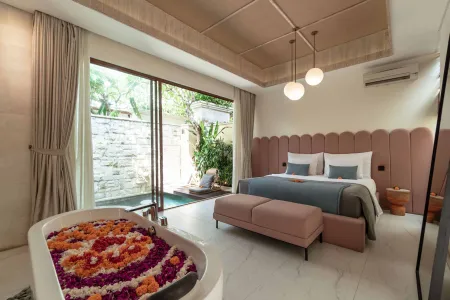 Luxurious Balinese bedroom with plush pink headboard bed, petal-filled bathtub, and tropical garden views through sliding doors.