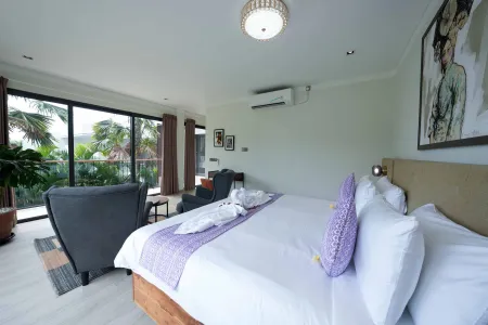 Spacious modern tropical bedroom with king bed, purple bedding, armchair, and balcony views of lush palm trees.