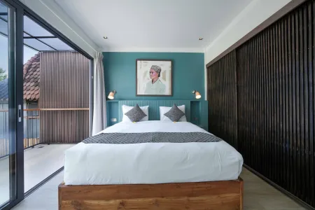 Modern Balinese-style bedroom with wooden platform bed, white linens, teal portrait wall art, and sliding glass doors to balcony.