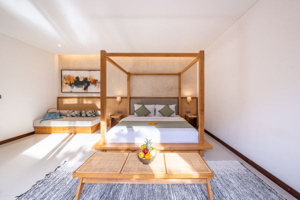 Elegant tropical bedroom with wooden four-poster bed, plush daybed, abstract wall art, and pineapple centerpiece on woven table.