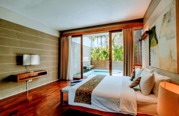 Luxurious tropical bedroom in a Bali villa with king-size bed, sliding doors to private infinity pool, and lush greenery.