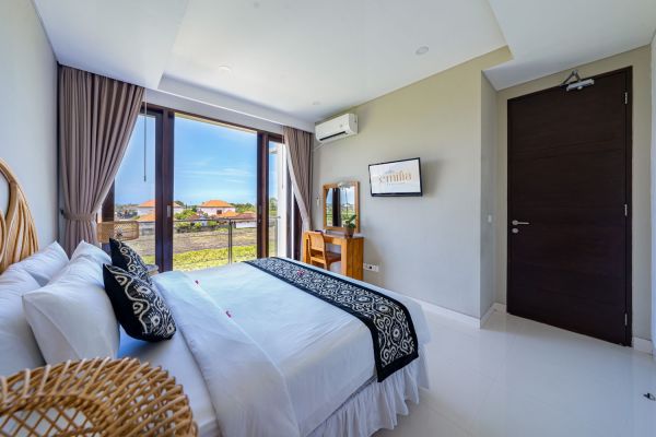 Spacious tropical bedroom with king bed, wooden accents, and balcony view of lush green fields.