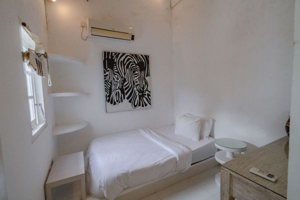 Cozy minimalist single bedroom with white walls, zebra stripe wall art, single bed, floating shelves, and wooden side table.