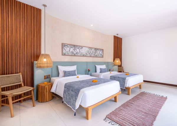 Cozy Balinese twin bedroom with wooden slat walls, rattan chair, blue bedspreads, and orange frangipani flowers.