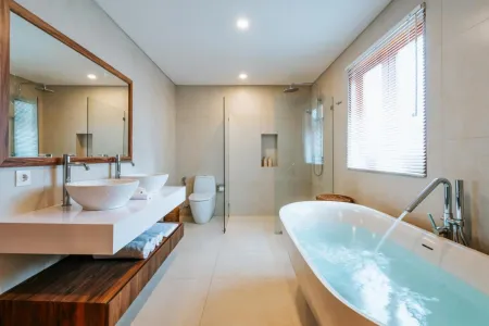 Modern luxury bathroom featuring a freestanding soaking tub, double white sinks on wooden vanity, glass shower enclosure, and soft natural light. - Bali Villas