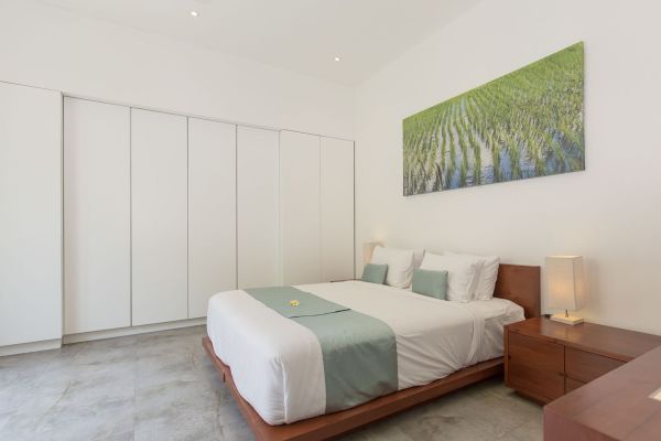 Modern minimalist bedroom with low wooden platform bed, green accents, white wardrobe, and large wall art of lush rice terraces.