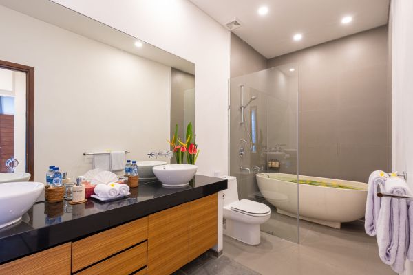 Modern luxury bathroom with freestanding bathtub filled with petals, double vessel sink vanity, glass shower, and tropical accents. - Bali Villas