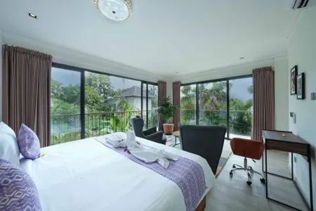 Luxurious tropical villa bedroom with king bed, purple accents, seating area, and panoramic balcony views of lush greenery and lake.