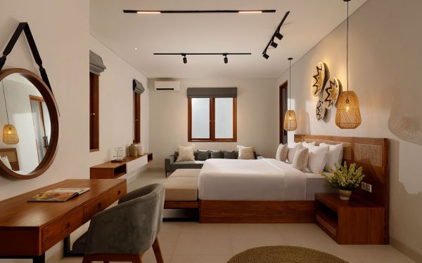 Spacious modern tropical bedroom with wooden bed, desk, mirror, and woven wall hangings under warm pendant lights. - Bali Villas