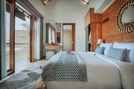 Luxurious Balinese villa bedroom with king bed, wooden accents, round mirror, and tropical balcony view. - Bali Villas