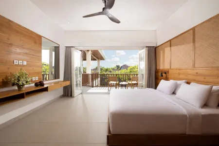 Spacious luxury Bali villa bedroom with king bed, wooden accents, ceiling fan, and open balcony overlooking tropical gardens.