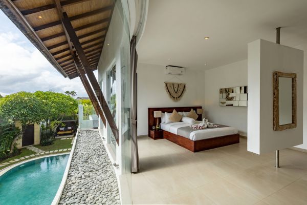 Luxurious open-plan Balinese bedroom with king bed, sliding glass doors overlooking infinity pool and tropical garden.