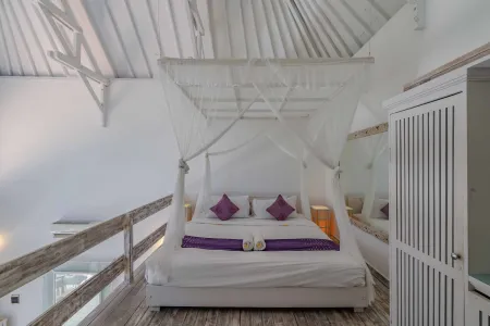 Elegant white canopy bed with purple pillows in a Balinese villa bedroom, featuring wooden beams and balcony railing.