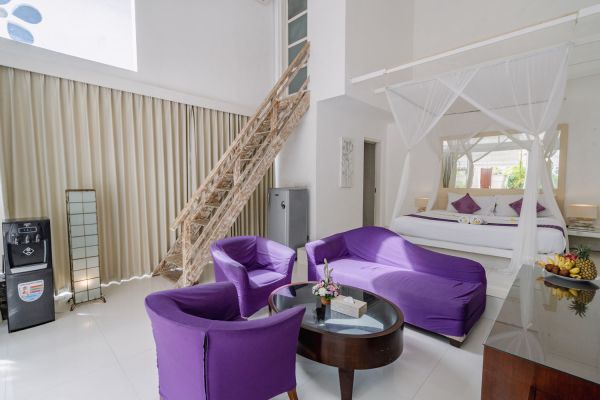 Spacious Balinese-style bedroom with purple velvet sofa and chairs, canopy bed, wooden staircase, and tropical decor. - Bali Villas