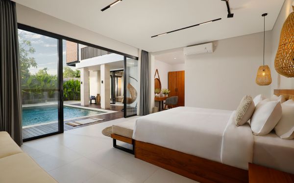 Luxurious modern bedroom in a Bali villa with sliding glass doors opening to a private infinity pool and tropical garden.
