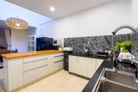 Modern white kitchen featuring wooden island, black granite counters, pull-out faucet sink, and woven pendant light. - Bali Villas