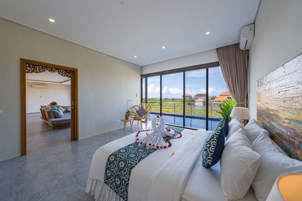 Luxurious Bali villa bedroom with king bed, romantic towel swan and rose petals, and panoramic rice field view through floor-to-ceiling windows.