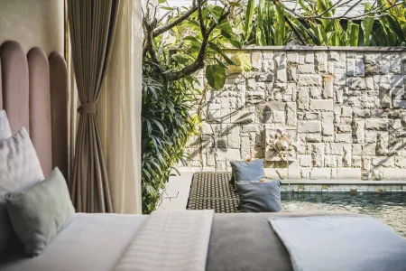Luxurious tropical bedroom with plush bed overlooking a private turquoise pool, lush greenery, and stone wall.