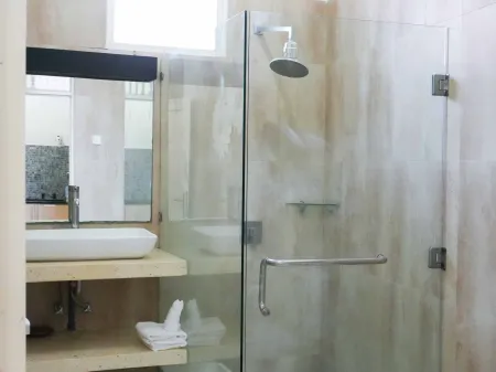 Modern bathroom with glass shower enclosure, rain showerhead, and wooden vanity sink. - Bali Villas