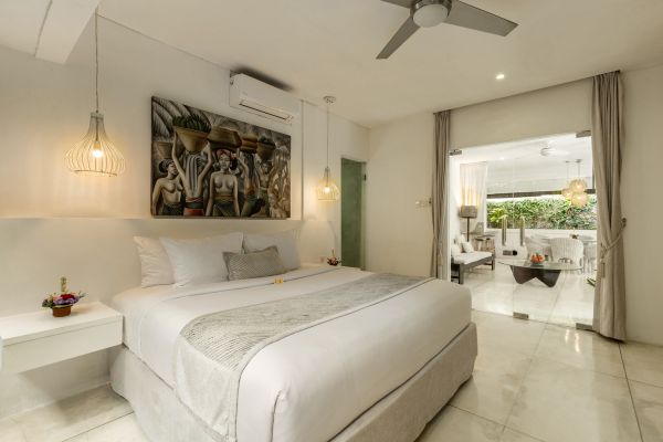 Luxurious white king bedroom in Bali villa with Balinese artwork, pendant lamps, ceiling fan, and open doors to tropical patio.