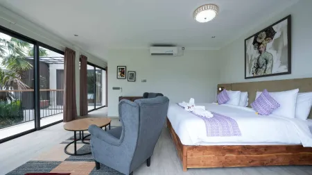 Spacious tropical resort bedroom with king bed, purple accents, gray armchair, and garden balcony view.