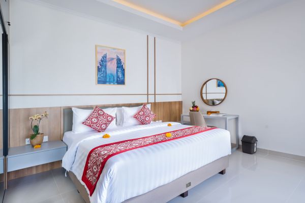 Elegant Balinese bedroom with white king bed, red embroidered runner, orchids, and round mirror against ocean-view balcony.