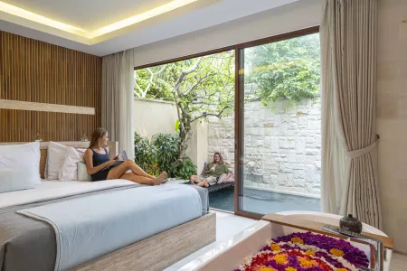 Luxurious Balinese villa bedroom with a woman reading on the bed, open garden views, and a petal-filled bathtub.