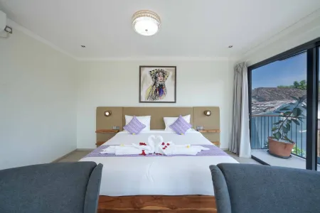 Luxurious hotel bedroom with king bed adorned in purple orchids and rose petals, modern decor, and sliding doors to a tropical balcony view.