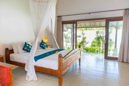 Luxurious wooden canopy bed in a tropical bedroom with open sliding doors revealing lush greenery and sea view.