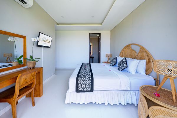 Serene Balinese bedroom with rattan headboard, white linens, wooden desk, orchids, and wall-mounted TV.