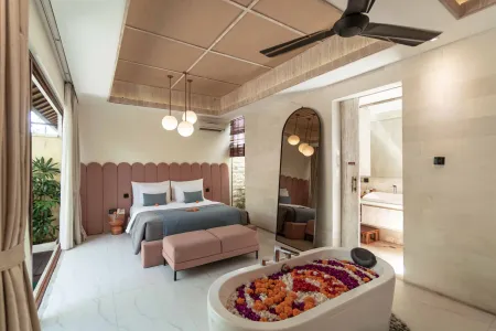 Luxurious Balinese-style bedroom suite featuring a petal-filled bathtub, king bed with pink headboard, and tropical decor.