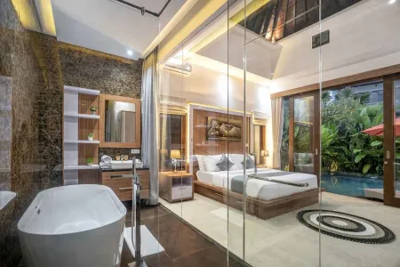 Luxurious Balinese villa bedroom-bathroom suite with king bed, freestanding tub, wooden accents, and private pool view through glass doors.