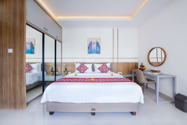 Serene Bali hotel bedroom with king bed, mirrored wardrobe, wooden desk, and tropical red accents.