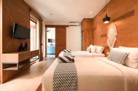 Spacious tropical bedroom with two white queen beds, wooden zigzag walls, mounted TV, dreamcatcher decor, and sliding doors to balcony.