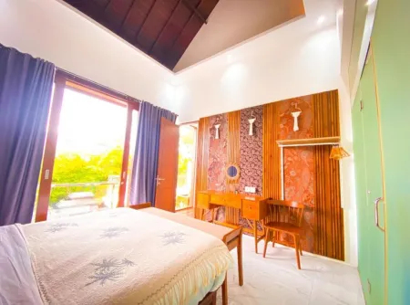 Spacious Balinese-style bedroom with wooden ceiling and accents, king bed, vanity desk, and sliding glass doors to tropical garden view.