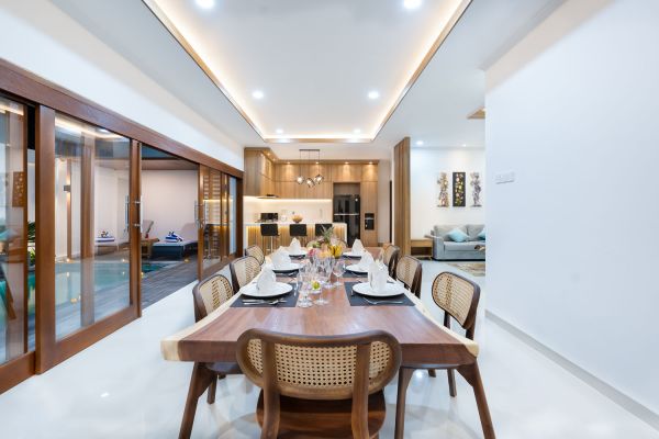 Spacious modern kitchen and dining area with wooden table set for meals, open cabinetry, and sliding glass doors to pool. - Bali Villas