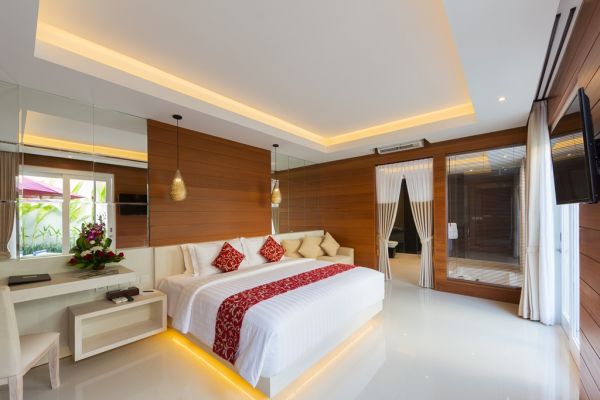 Luxurious Balinese villa bedroom with wooden paneling, king bed with red accents, ambient LED lighting, and tropical flowers.