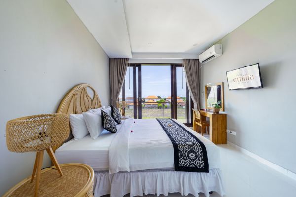 Cozy Bali villa bedroom with king bed, bamboo accents, balcony view of tropical palms, and modern amenities.