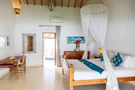 Spacious tropical beach villa bedroom with king bed under sheer mosquito net, wooden furniture, open balcony doors, and ocean view.